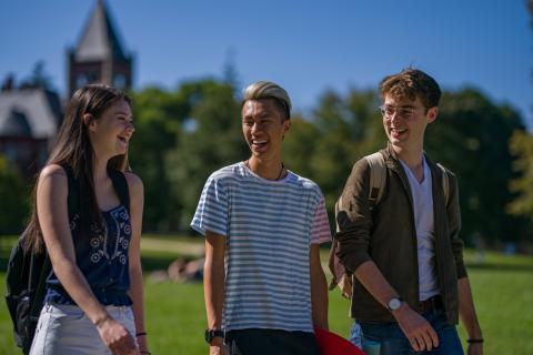 Three students walking and talking with T-Hall in the background